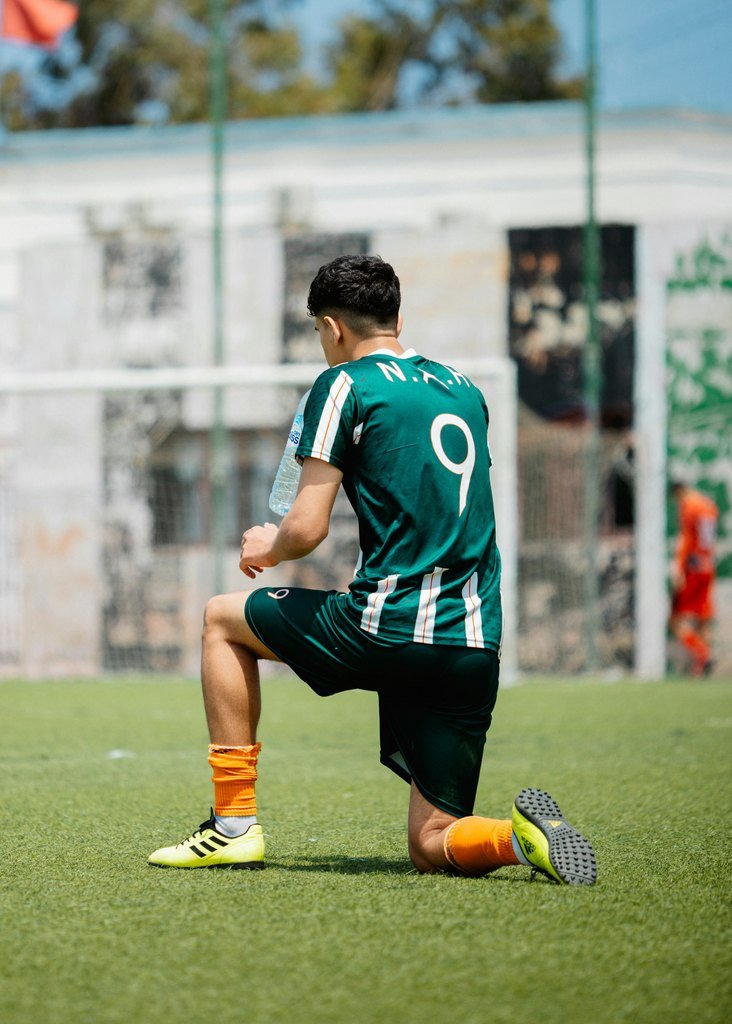 Player in a green number 9 kit kneeling on the pitch