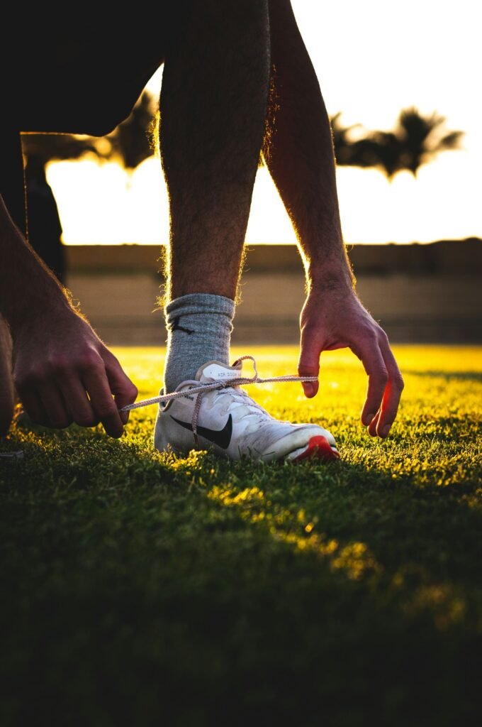 Player lacing up white boots on the grass at sunset